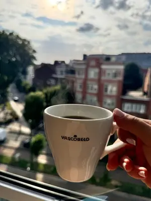 a person holding a cup of coffee in front of a window at LUYS Apartment in Brussels