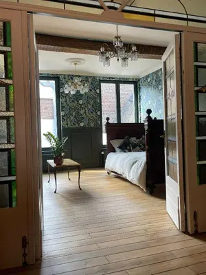 a bedroom with a bed and a table and windows at La Petite Foret Art Deco Apartment in Brussels in Brussels
