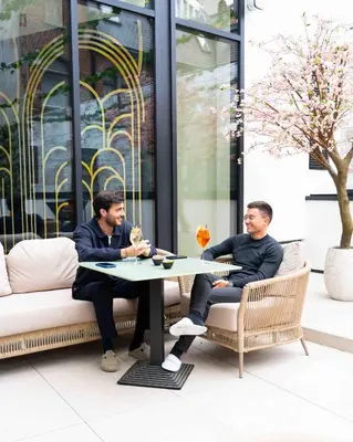 two men sitting at a table in front of a building at The Liman Hotel in Brussels