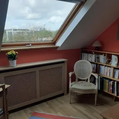 a room with a window and a chair and a book shelf at B&B Woluwé in Brussels