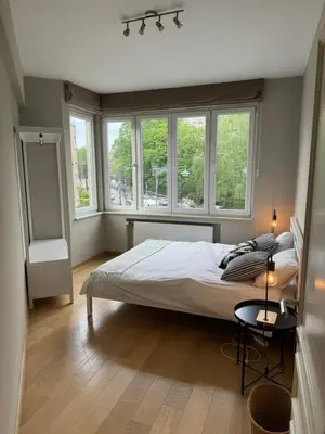a bedroom with a bed and two windows at Appartement Ixelles 2 chambres, 3 lits in Brussels