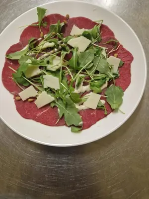 a white plate with a pizza with cheese and greens at De Baolse Herberg in Baarle-Hertog