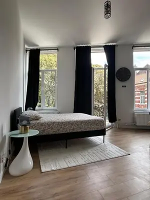 a bedroom with a bed and a table and windows at Studio Nour in Brussels