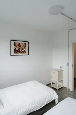 a white bedroom with a bed and a night stand at De Logé in Oud-Turnhout