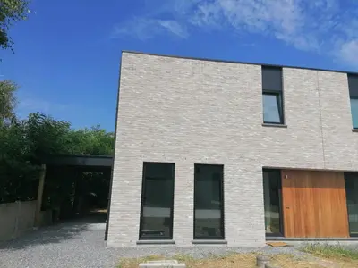 a white brick building with a wooden door at Dunehill in Balen
