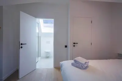 a white bedroom with a bed and a bathroom at Märch - Mechelen Goat 14 in Mechelen