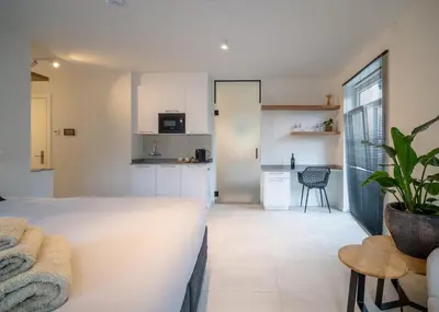 a bedroom with a white bed and a kitchen at Mavue kamer met terras in Mechelen