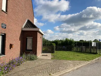 a brick building with a grass yard next to a fence at Vakantiewoning de Huismus in Oud-Turnhout