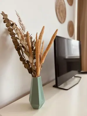 a green vase with flowers in front of a computer monitor at Flat moderne et lumineux in Brussels