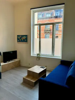 a living room with a blue couch and a large window at Studio avec chambre en mezzanine in Brussels