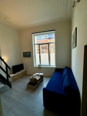 a living room with a blue couch and a window at Studio avec chambre en mezzanine in Brussels