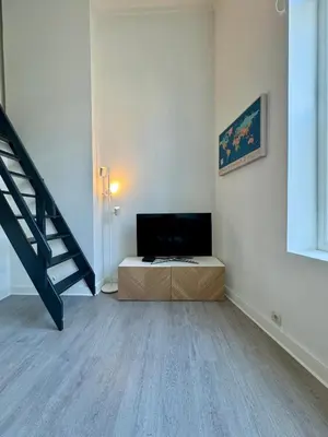 a living room with a flat screen tv and a staircase at Studio avec chambre en mezzanine in Brussels
