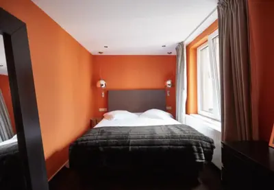 a bedroom with a bed with orange walls and a window at Villa Sablon in Brussels