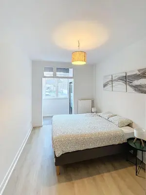 a white bedroom with a bed and a chandelier at Magnifique appartement une chambre in Brussels