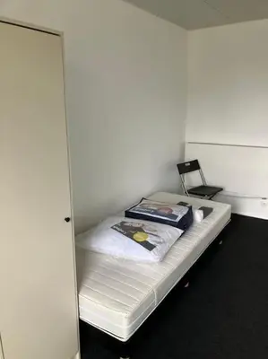a small white room with a bed with a chair at Expats House 10 Stabroek Belgium in Stabroek