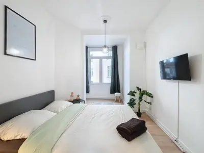 a white bedroom with a large bed and a tv at Porte de Namur in Brussels