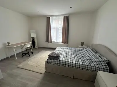 a white bedroom with a bed and a desk at Appartement confortable avec garage premier étage sans terrasse in Brussels