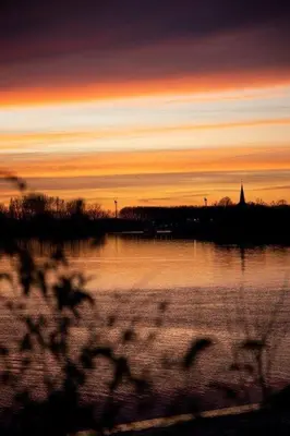 a sunset over a lake with a church in the distance at Waterfront vacation home in Sint-Amands