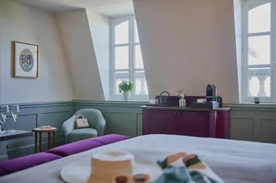 a bedroom with a bed and two chairs and windows at Faubourg 21 in Brussels