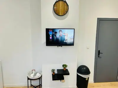 a flat screen tv on a white wall with a clock at Apparts de standing Bruxelles Brady Muandaz in Brussels