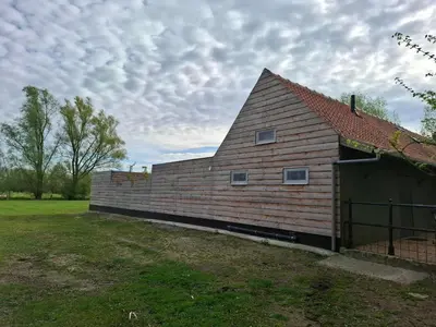 a barn with a brick wall next to a field at Huis-Chalet aan Puyenbroeck in Wachtebeke