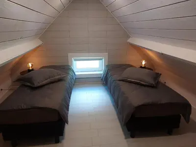 two beds in a attic room with a window at Huis-Chalet aan Puyenbroeck in Wachtebeke