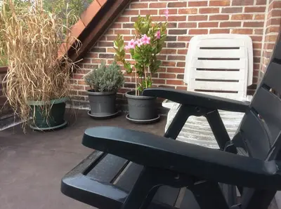 a black bench sitting on a patio with potted plants at Cosy attic apartment, terrace, 1 bedroom south, 1 double bed for 2, plus single bed if 3 guests in Opdorp