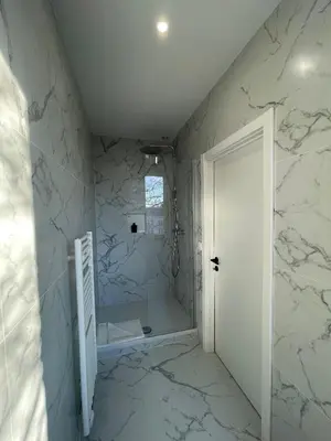 a bathroom with white marble walls and a walk in shower at La Perla Appartements in Brussels