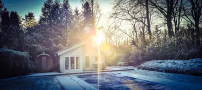 a house in the snow with the sun shining on it at Cozy tiny house with swimming pool & outdoor sauna in Waasmunster