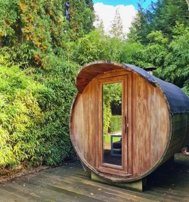 a large wooden barrel with a door in a garden at Cozy tiny house with swimming pool & outdoor sauna in Waasmunster