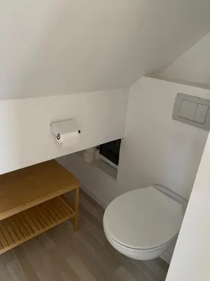 a bathroom with a white toilet and a wooden table at Sous un toit perché in Grez-Doiceau