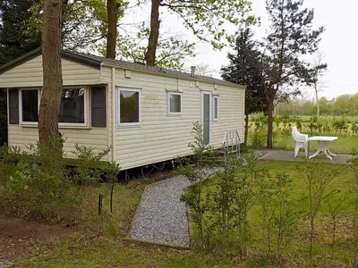 a white tiny house with a bench in a yard at Verblijfpark De Brem in Lille
