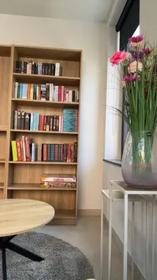 a vase of flowers on a table with a book shelf at Sœur in Berlare