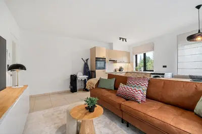 a living room with a brown couch and a kitchen at Comfort aan stadsrand Gent, vlakbij Natuurgebied in Ghent