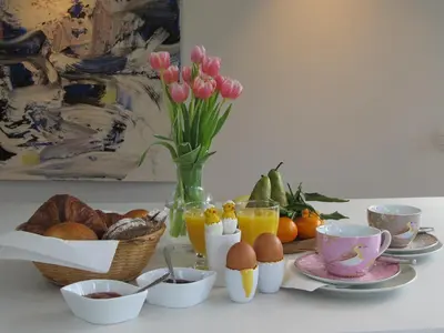a breakfast table with eggs bread and oranges and a vase of flowers at B&B Zoersel in Zoersel