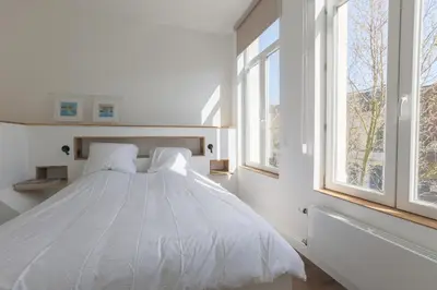 a bedroom with a white bed with two windows at Southside Suites in Antwerp