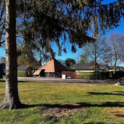 a building in a park with a tree in the foreground at Trekkershutten - Camping Groenpark in Zele