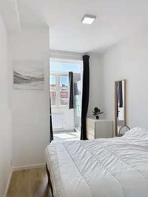 a white bedroom with a bed and a window at Élégant appartement une chambre in Brussels