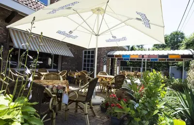 a patio with tables and chairs and an umbrella at Hotel Pacific in Weelde