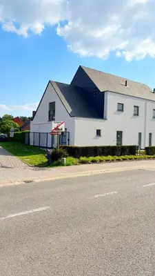 a white building with a black roof next to a street at Bruggeske aan't bos in Mol