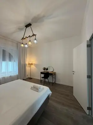 a white bedroom with a large bed and a desk at Oasis Apartament in Brussels