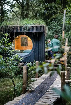 a hut with a grass roof on a wooden bridge at Cabins in the woods with wellness in Brasschaat