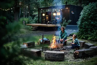 two children sitting around a fire in front of a cabin at Cabins in the woods with wellness in Brasschaat