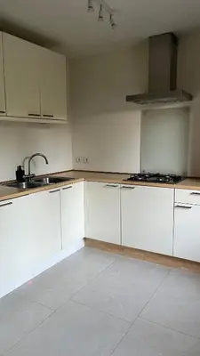 an empty kitchen with white cabinets and a sink at Cozy apartment with garden in Ghent