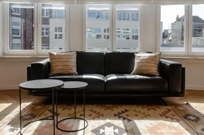 a black leather couch in a living room with windows at Bellavista Luxe Apartment with Leie View in Ghent