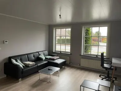 a living room with a black couch and two windows at Rent and Relax Geel in Geel