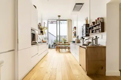 a kitchen with white cabinets and a wooden floor at Cozy Room with Garden in Brussels