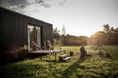 a man sitting next to a picnic table in a field at Gorgeous Off-Grid Tiny House Near Antwerp, Belgium in Wuustwezel