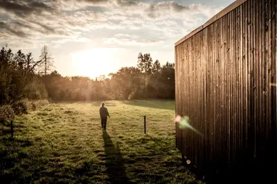 a man walking in a field next to a building at Gorgeous Off-Grid Tiny House Near Antwerp, Belgium in Wuustwezel