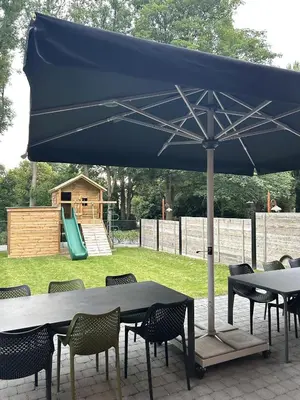 a blue umbrella on a table with chairs and a playground at Comfortabele groepswoning voor 8 met ruimte tuin in Turnhout